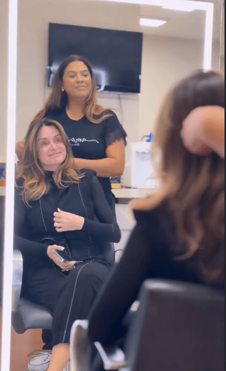 Cliente sorrindo no espelho com a profissional após o penteado